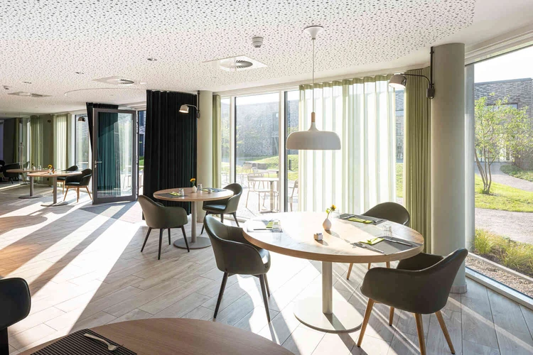Heller Speisesaal mit runden Tischen und Blick in den Innenhof